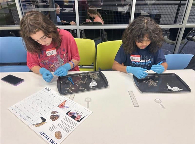 two children sitting at table working on science kits