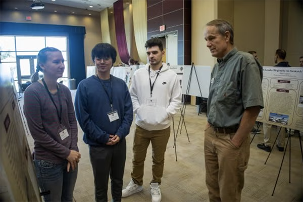 photo of professor and students talking among posters on easels