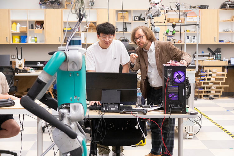 two men in front of computer looking at robot