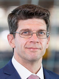man with glasses and white shirt, blue jacket, pink tie smiling at camera