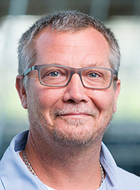 man with short gray hair and glasses in light blue shirt smiling