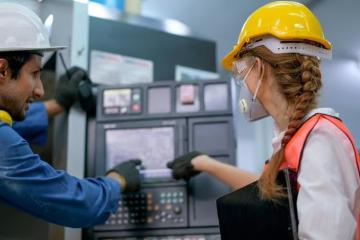 two people in hard hats looking at a control panel in a lab, from behind