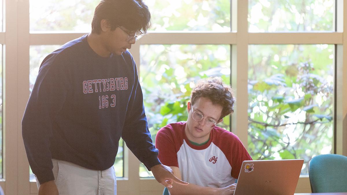photo of two male students looking at a book in front of a windo