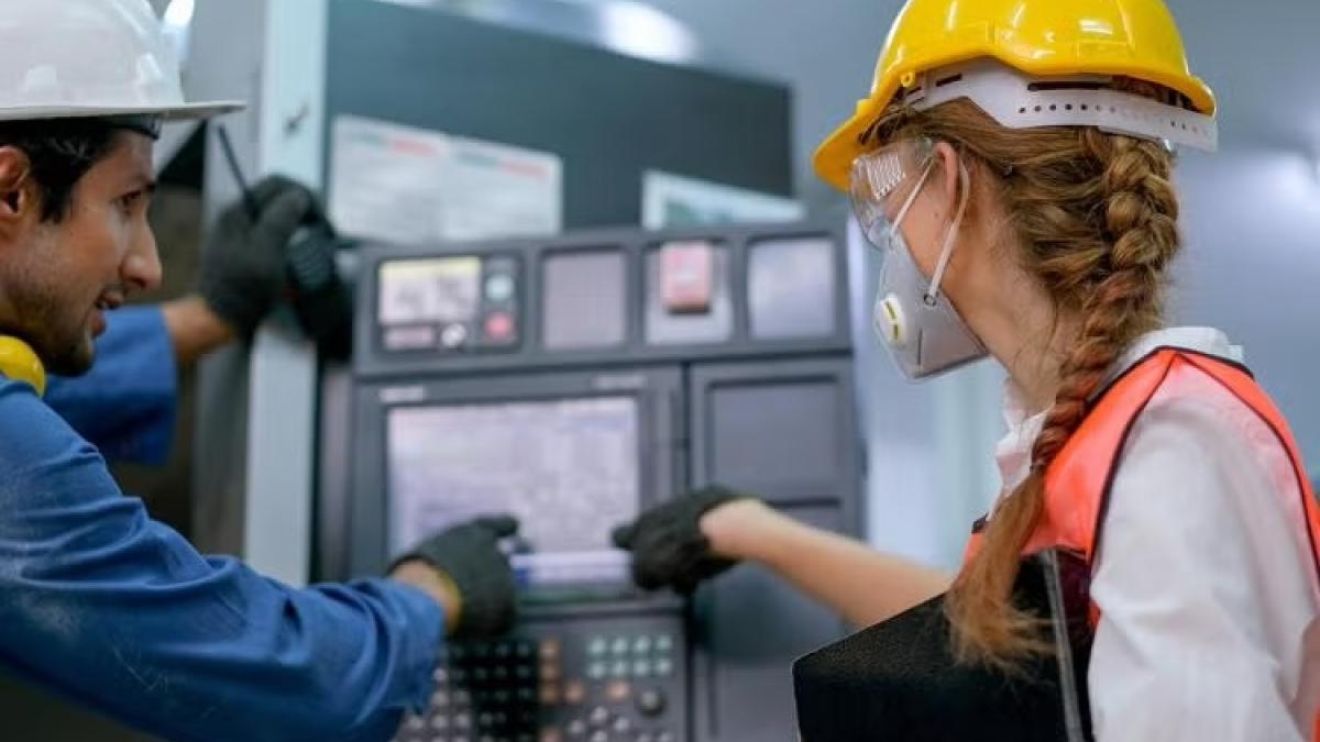 two people in hard hats looking at a control panel in a lab, from behind