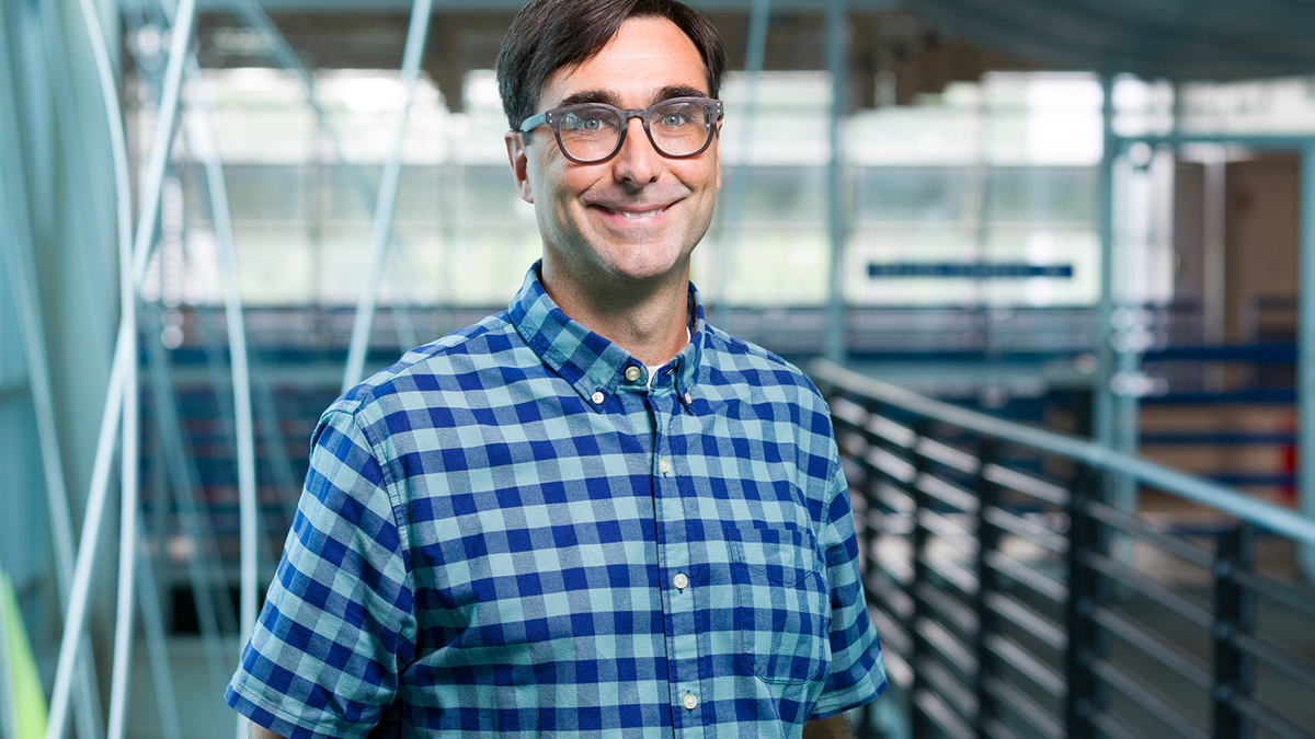 smiling man with short dark hair and glasses in blue plaid shirt