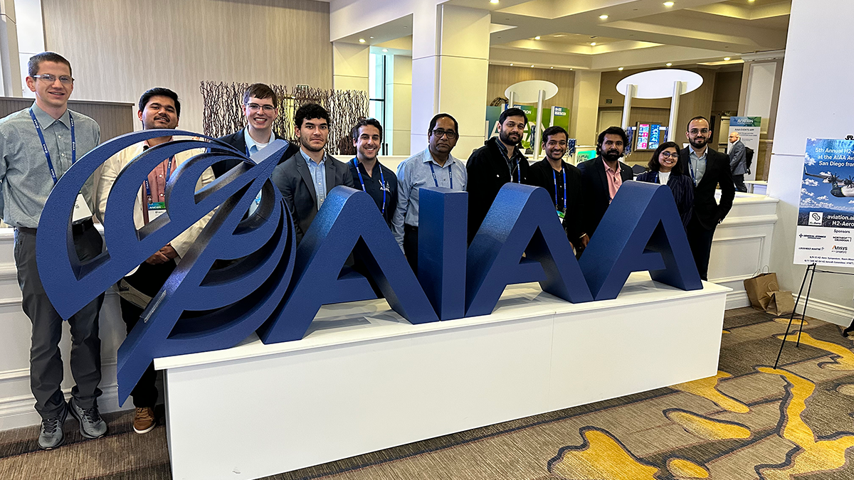 group of people in suits standing side by side behind large blue AIAA logo