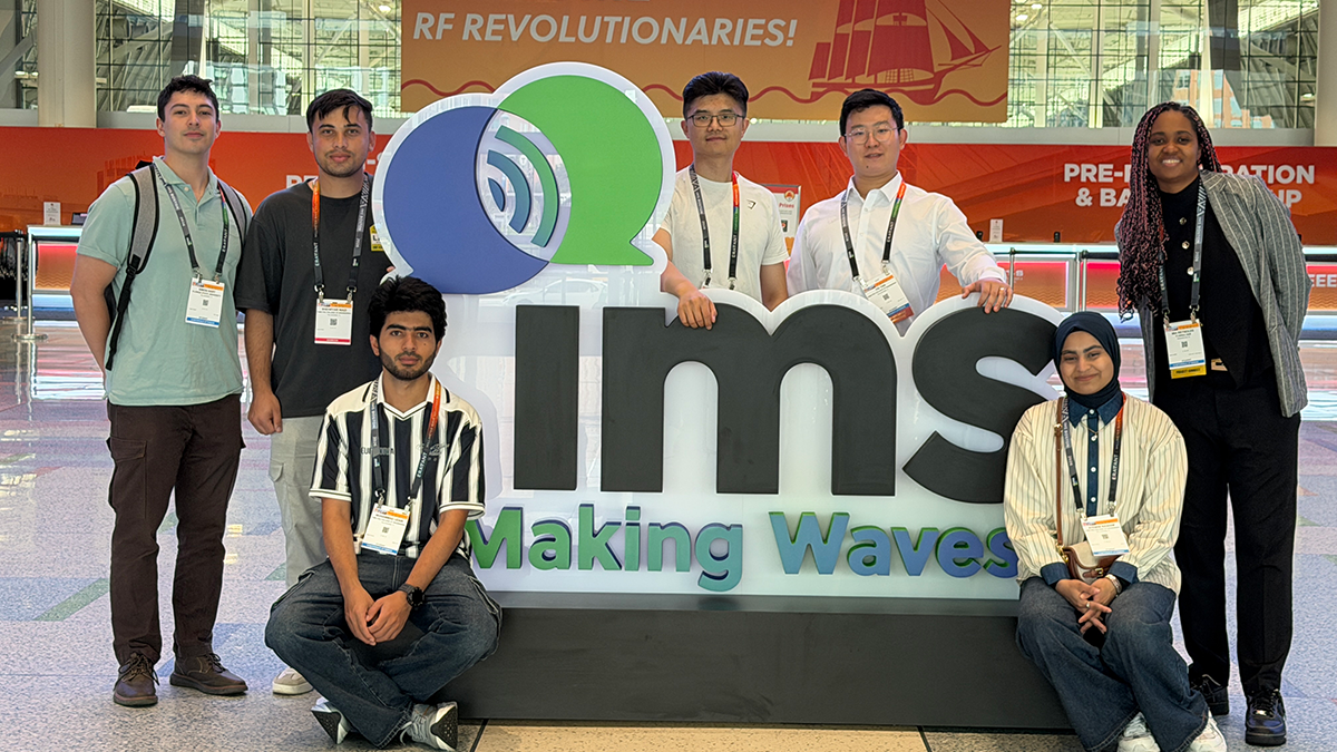group of students stand behind and around a large logo of IMS making waves in text