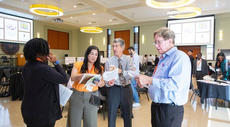 Four participants at the 2024 R-SEAT Conference stand engaged in conversation
