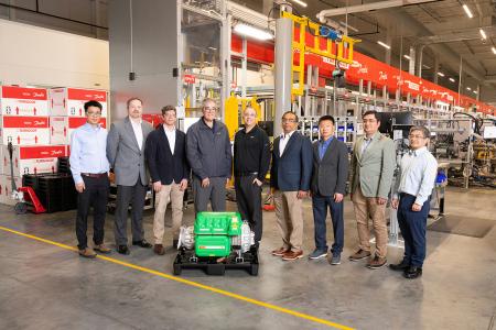 group of men standing in front of green machine on floor of warehouse