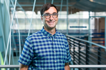 smiling man with short dark hair and glasses in blue plaid shirt