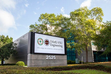 Exterior sign reading "FAMU-FSU Engineering, One college, two universities, unlimited opportunity" outside the college's building at 2525, with trees and a partly cloudy sky in the background.
