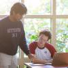 photo of two male students looking at a book in front of a windo