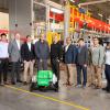 group of men standing in front of green machine on floor of warehouse