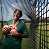 A student athlete laughs while holding a throwing weight and medals inside an outdoor throwing cage