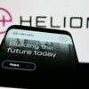 Photo of Mobile phone with website of US fusion power company Helion Energy Inc. in front of business logo. Focus on top-left of phone display