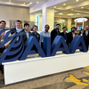 group of people in suits standing side by side behind large blue AIAA logo