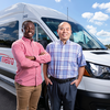 Two smiling men stand in front of a white StarMetro paratransit van. One wears a red checkered shirt with his arms crossed, while the other wears a blue plaid shirt with his hands in his pockets.