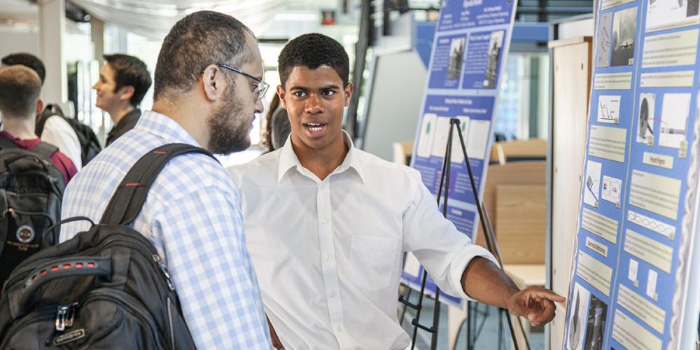 Young student explaining his project while pointing to his poster presentation